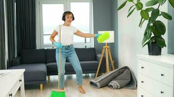 femme dans écouteurs nettoyage le maison et ayant amusement dansant avec une balai et un gant de toilette. video