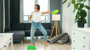 Woman in headphones cleaning the house and having fun dancing with a broom and washcloth. video