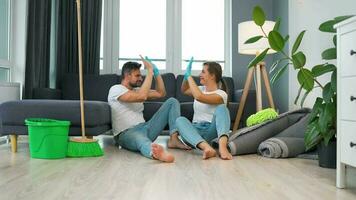 Tired couple sits on the floor in a room and high five each other after they finish cleaning the house video