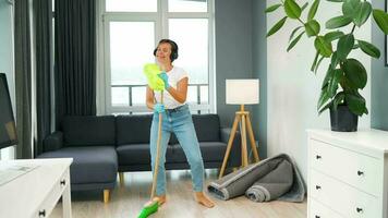 Woman in headphones cleans the house and have fun singing with a broom like a star at a concert video