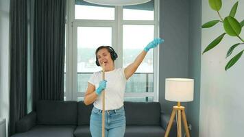 Woman in headphones cleans the house and have fun singing with a broom like a star at a concert video