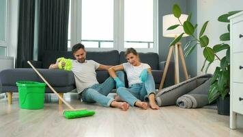 Tired couple sits on the floor in a room and high five each other after they finish cleaning the house video