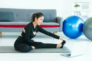 Asian young healthy woman wearing sportware online fitness training with laptop at home photo