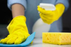 Woman's hands in rubber gloves hold a cleaner and wipe the table with a rag. Concept of spring cleaning. Housekeeping concept. Close-up. Selective focus. photo