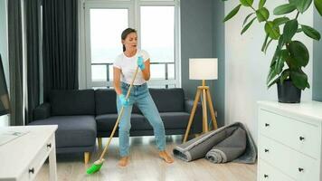 femme dans écouteurs nettoyage le maison et ayant amusement dansant avec une balai et un gant de toilette video