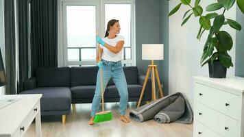 kvinna i hörlurar rengöring de hus och har roligt dans med en kvast och tvättlapp video