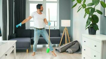 Man in headphones cleaning the house, fooling around and having fun dancing and singing with a broom video