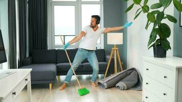 Man in headphones cleaning the house and fooling around with a broom video