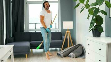 Man in headphones cleaning the house and fooling around with a broom video