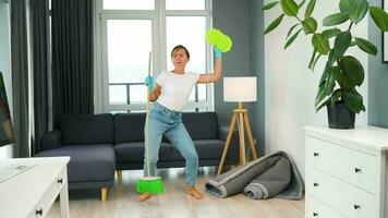 mulher dentro fones de ouvido limpeza a casa e tendo Diversão dançando com uma vassoura e toalha video