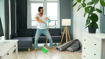 Man in headphones cleaning the house and fooling around with a broom video