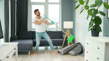 Man in headphones cleaning the house, fooling around and having fun dancing and singing with a broom video