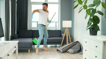 hombre en auriculares limpieza el casa, engañando alrededor y teniendo divertido bailando y canto con un Escoba video