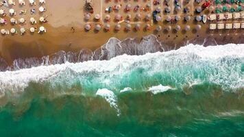 Aerial view of the sea, sandy beach, sun umbrellas and sunbeds, unrecognizable people. Beautiful vacation and tourism video