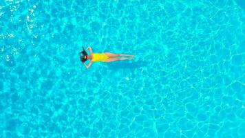 Aerial view of a woman in yellow swimsuit swimming in the pool. Summer lifestyle video