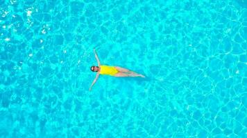 Aerial view of a woman in yellow swimsuit swimming in the pool. Summer lifestyle video