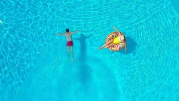 Haut vue de une couple ayant amusement dans le piscine, le homme nage et le femme mensonges sur un gonflable Donut video