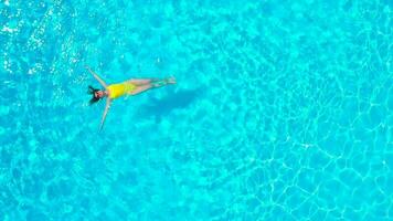 aéreo ver de un mujer en amarillo traje de baño nadando en el piscina. verano estilo de vida video