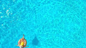 Aerial view of a woman in yellow swimsuit lying on a donut in the pool video