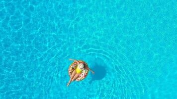 Aerial view of a woman in yellow swimsuit lying on a donut in the pool video