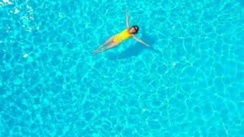 aéreo ver de un mujer en amarillo traje de baño nadando en el piscina. verano estilo de vida video