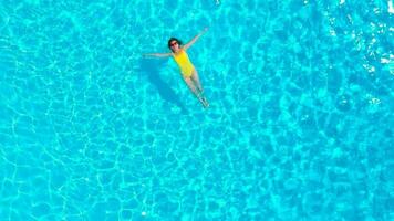 aéreo ver de un mujer en amarillo traje de baño nadando en el piscina. verano estilo de vida video