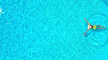 Aerial view of a woman in yellow swimsuit swimming in the pool. Summer lifestyle video