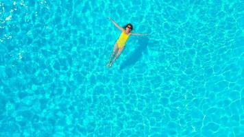 aéreo Visão do uma mulher dentro amarelo roupa de banho natação dentro a piscina. verão estilo de vida video