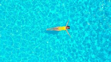 Aerial view of a woman in yellow swimsuit swimming in the pool. Summer lifestyle video