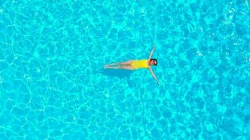 Aerial view of a woman in yellow swimsuit swimming in the pool. Summer lifestyle video