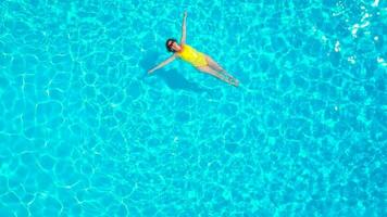 aéreo ver de un mujer en amarillo traje de baño nadando en el piscina. verano estilo de vida video