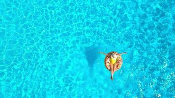 Aerial view of a woman in yellow swimsuit lying on a donut in the pool video