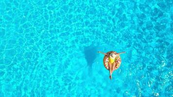 Aerial view of a woman in yellow swimsuit lying on a donut in the pool video