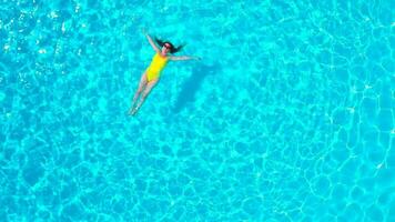 aéreo Visão do uma mulher dentro amarelo roupa de banho natação dentro a piscina. verão estilo de vida video