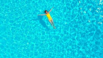 aéreo ver de un mujer en amarillo traje de baño nadando en el piscina. verano estilo de vida video