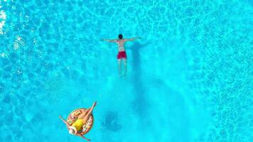 superiore Visualizza di un' coppia avendo divertimento nel il piscina, il uomo nuotate e il donna bugie su un gonfiabile ciambella video