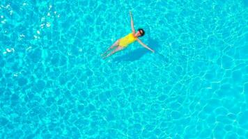 Aerial view of a woman in yellow swimsuit swimming in the pool. Summer lifestyle video