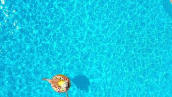 antenne visie van een vrouw in geel zwempak aan het liegen Aan een donut in de zwembad video