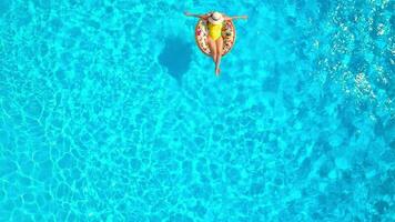 Aerial view of a woman in yellow swimsuit lying on a donut in the pool video