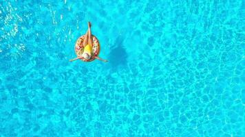 Aerial view of a woman in yellow swimsuit lying on a donut in the pool video