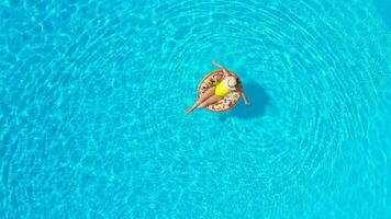 Aerial view of a woman in yellow swimsuit lying on a donut in the pool video