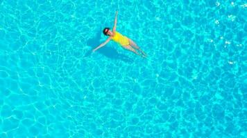 Aerial view of a woman in yellow swimsuit swimming in the pool. Summer lifestyle video