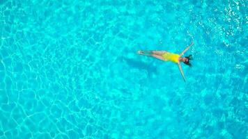 aéreo ver de un mujer en amarillo traje de baño nadando en el piscina. verano estilo de vida video