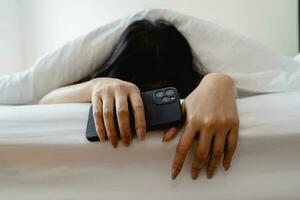 Woman with long black hair sleeping and holding mobile phone in white bed photo