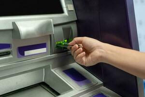 mano acerca de a insertar tarjeta a Cajero automático máquina Listo a retirar o transferir dinero. foto
