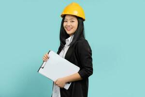 Portrait of happy smiling woman in yellow helmet and black suit She looks at the camera while standing and holding a clipboard with documents isolated over a green background. photo