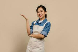 Portrait of cheerful Asian woman wearing apron on cream background photo