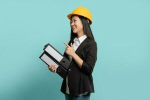 Portrait of Beautiful Asian engineer with hard hat pointing at copy space isolated on green background. photo