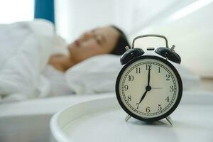 Asian woman resting in bed with alarm clock photo