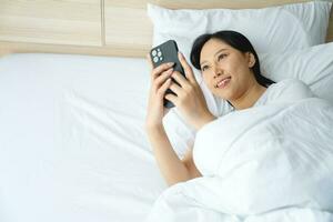 Closeup portrait of young sleepy exhausted woman lying in bed using smartphone photo